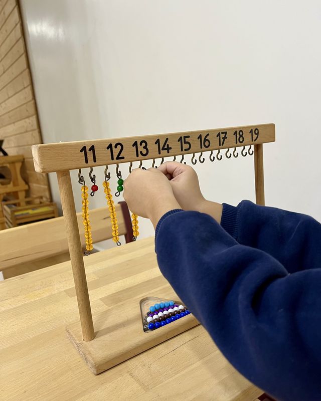 Montessori sınıfında boncuk askısıyla 11–19 sayılarını çalışan bir çocuğun elleri